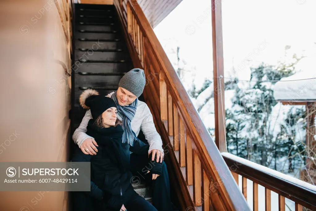 couple of young people a guy and a girl on the porch of a snow-covered wooden house in the winter mountains