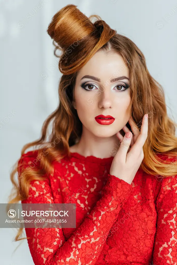 young girl with red hair in a bright red dress in a light room near a white wall