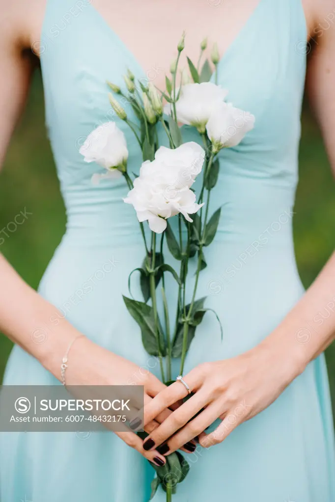 Happy girl in a turquoise long dress in a green park on a background of herbs, trees and rose bushes