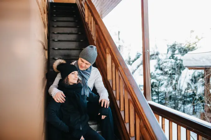 couple of young people a guy and a girl on the porch of a snow-covered wooden house in the winter mountains