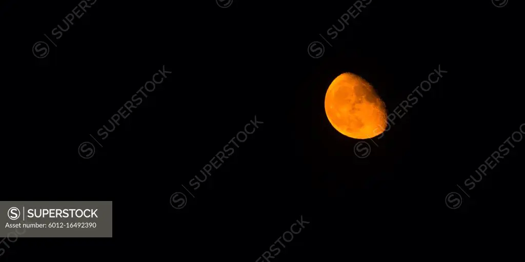 The moon takes on an orange hue in a dark night