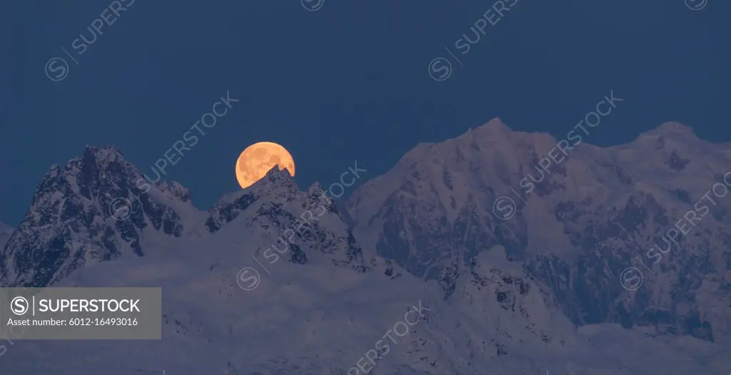 The moon emerges from behind the mountains in Denali