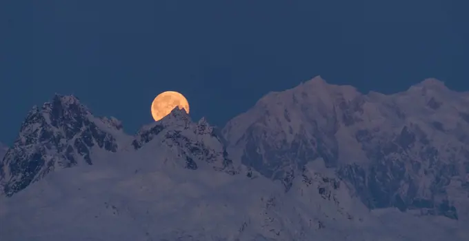 The moon emerges from behind the mountains in Denali