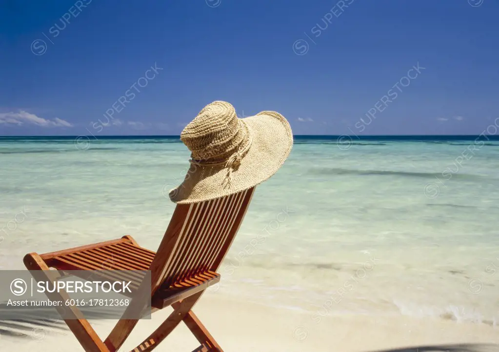 Sun hat resting on empty chair on tropical beach