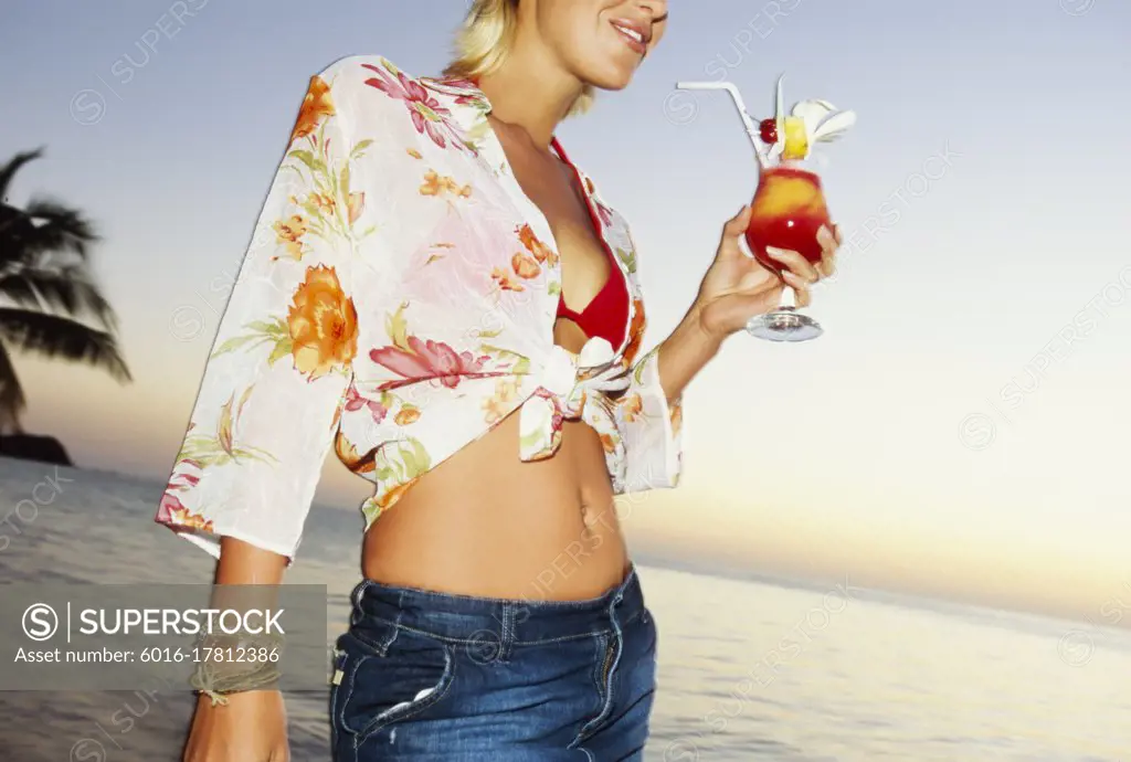 Young woman standing on tropical beach holding a cocktail