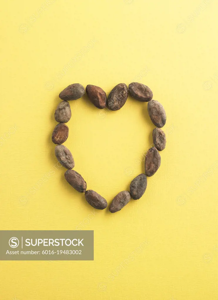 Raw cocoa beans shaped into a heart on yellow background