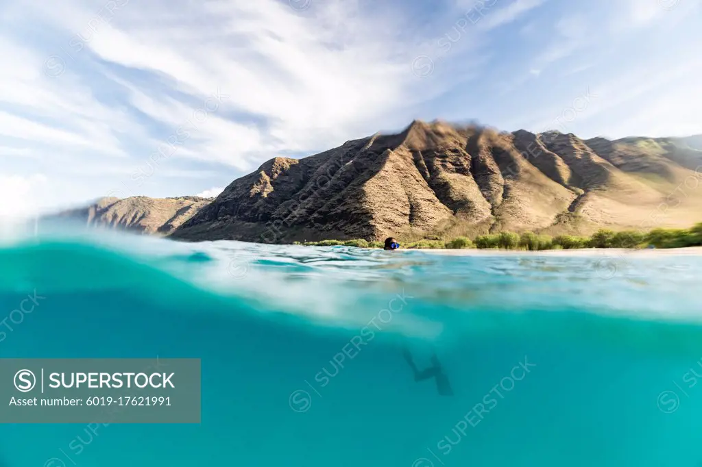 Snorkler bobs at the ocean surface with hawaii mountain background