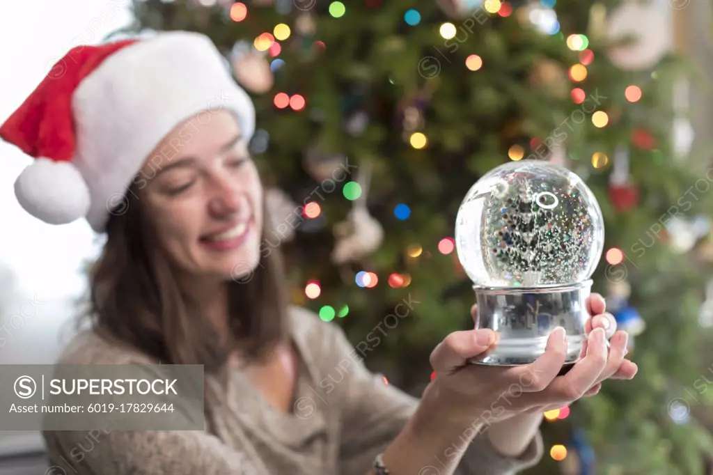 College-aged woman looking at Christmas snow-globe by Christmas Tree