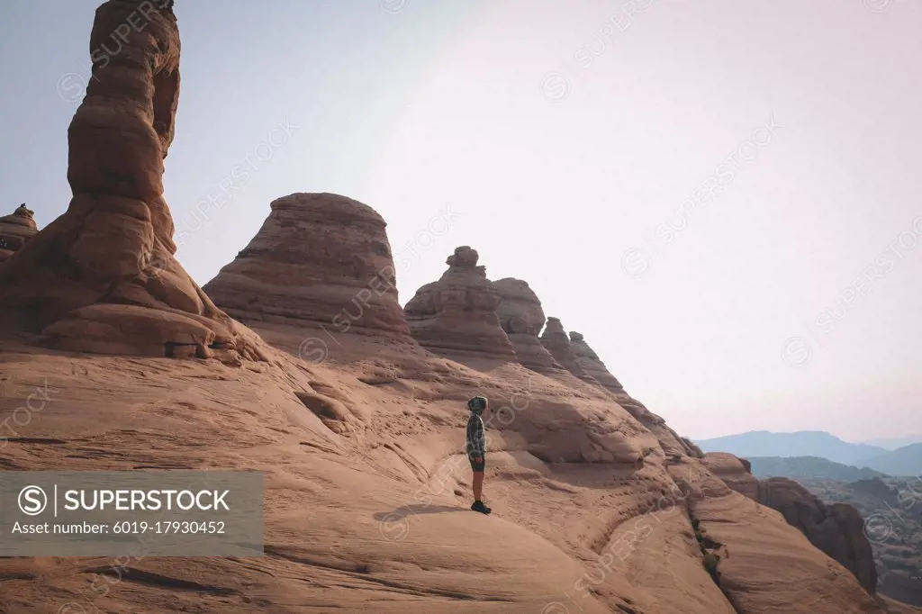 Young Boy Stands on a Cliff Edge Facing the Desert