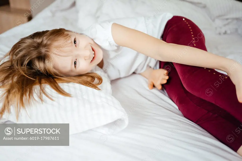 little girl laughs lying on a white bed