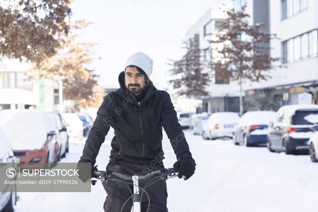 young man with beard riding  bike in snow on a street