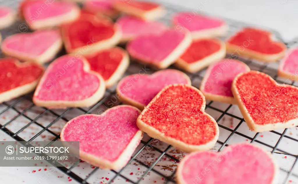 Close up of many decorated heart shaped cookies on cooling rack.