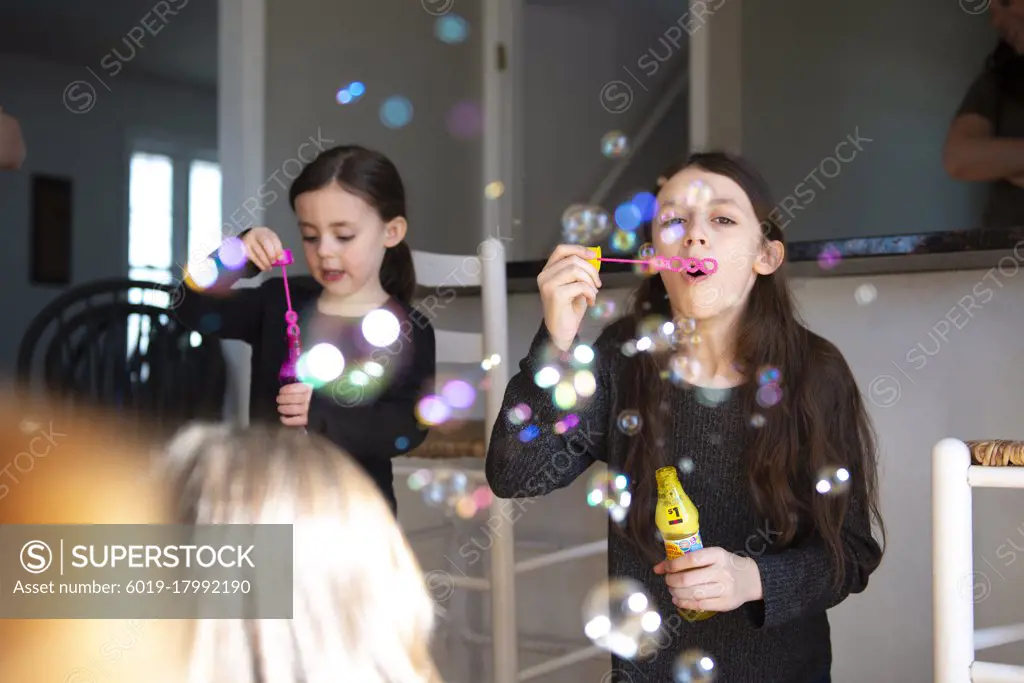 Cute little girls blowing bubbles in the kitchen with their family.