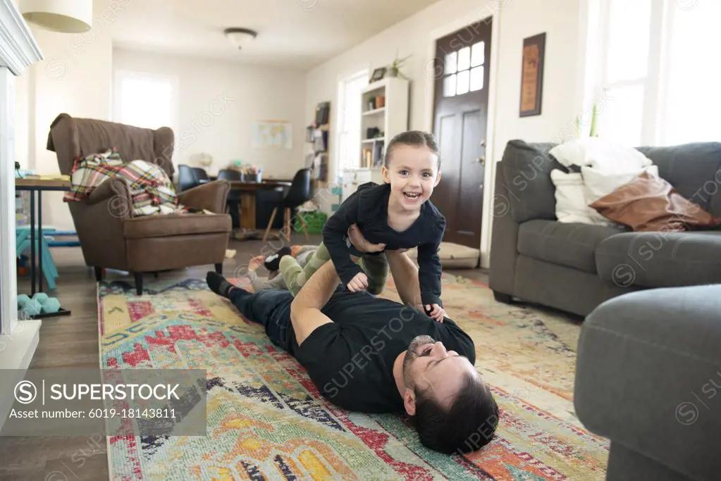 Father doing airplane with little girl on living room floor.