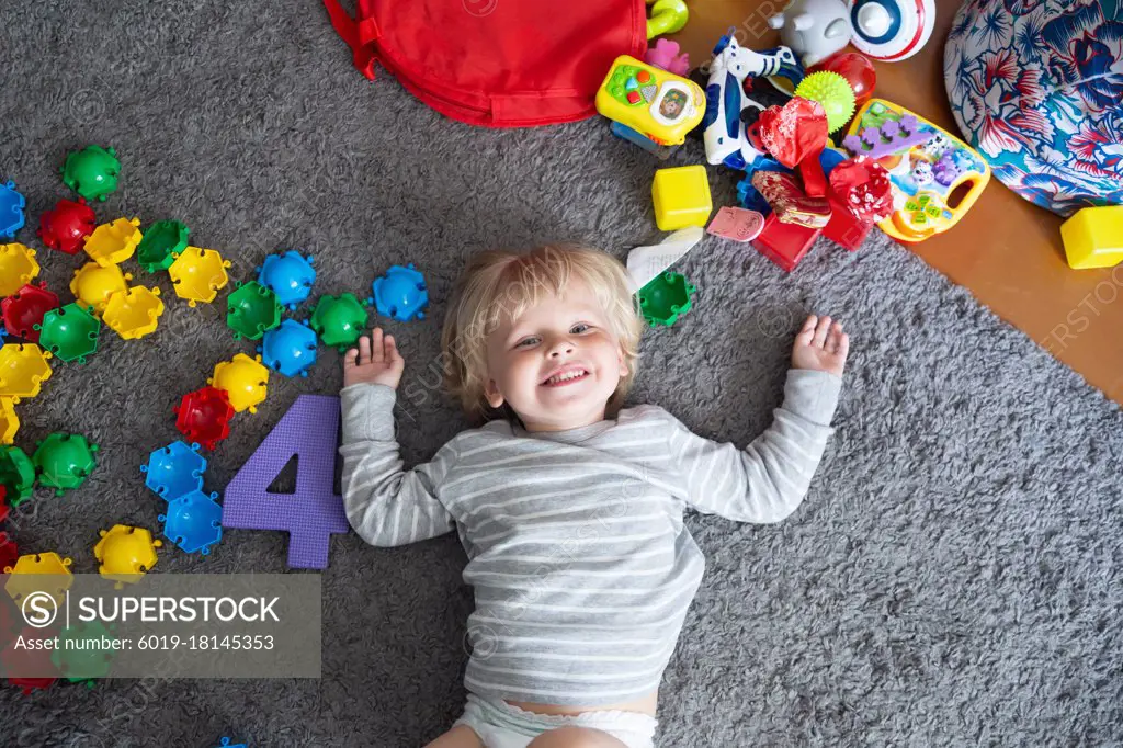 Happy blonde child lies on the floor with lots of toys