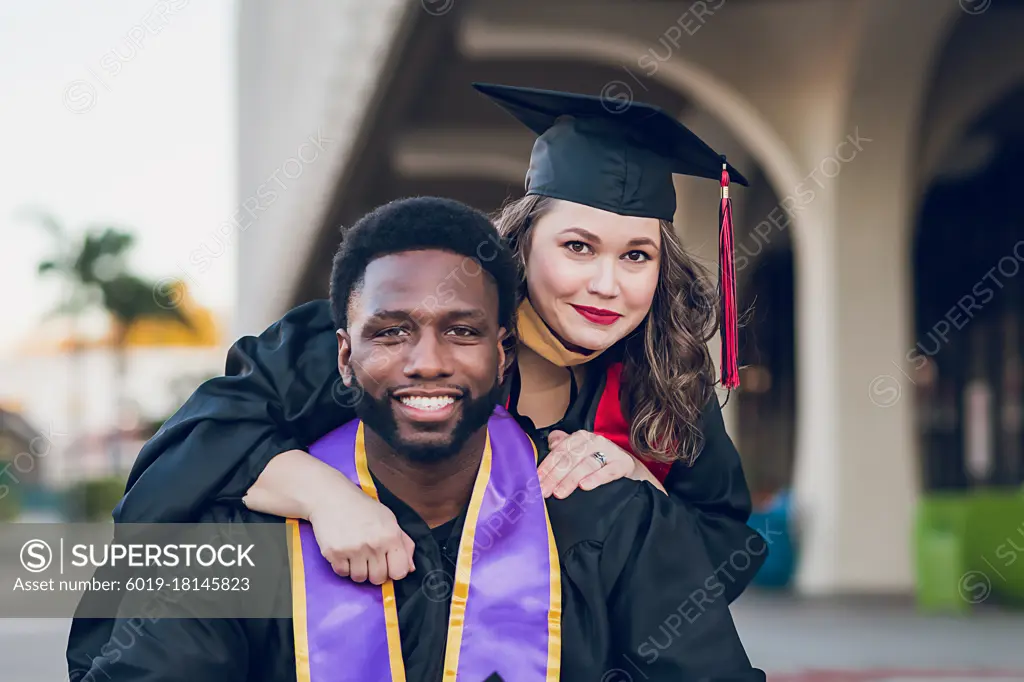 Young man & woman graduating college, wearing a graduation gown/cap.