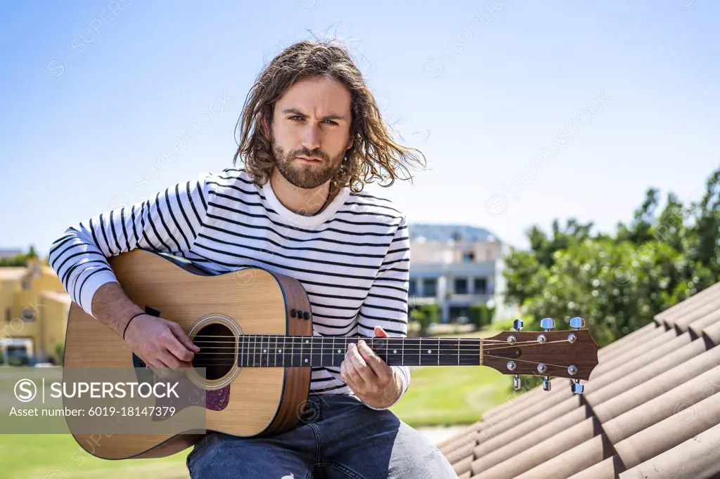 Attractive man with long hair playing acoustic guitar outdoors