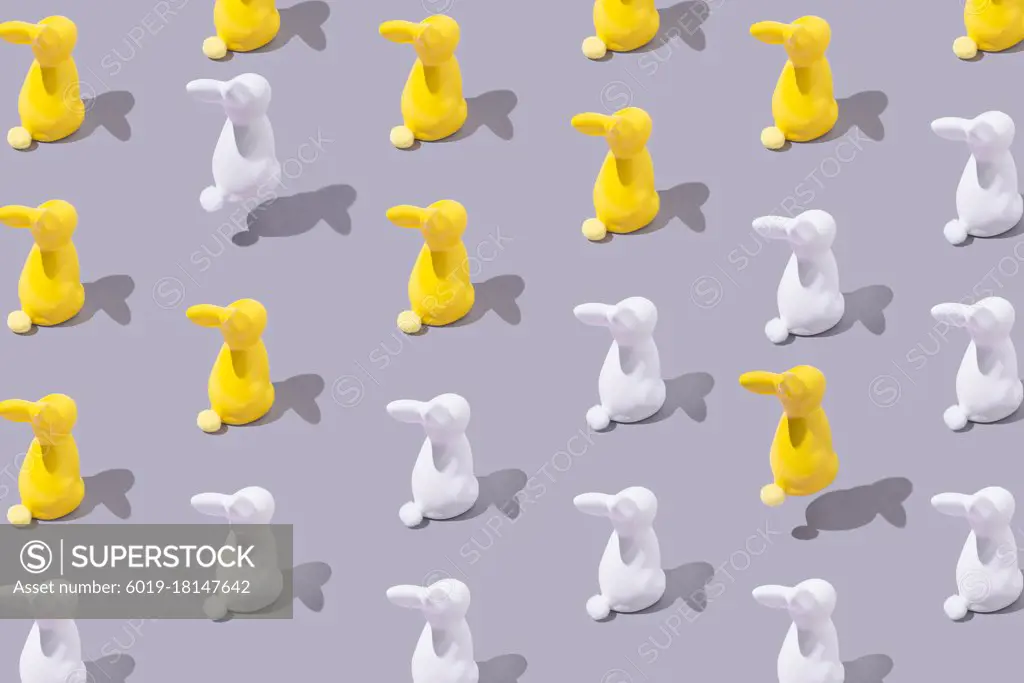 Creative pattern with yellow and white plastic bunny on grey bac