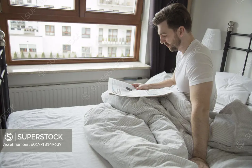 young man reading a newspaper with news in bed