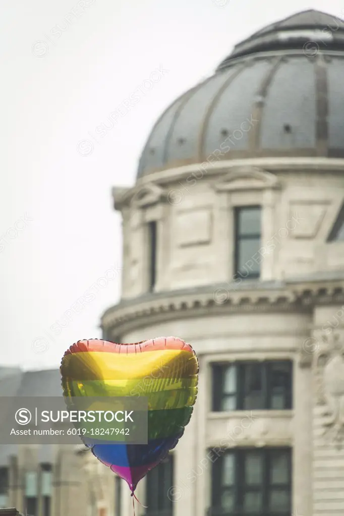 A heart shaped rainbow balloon floats in front of a building