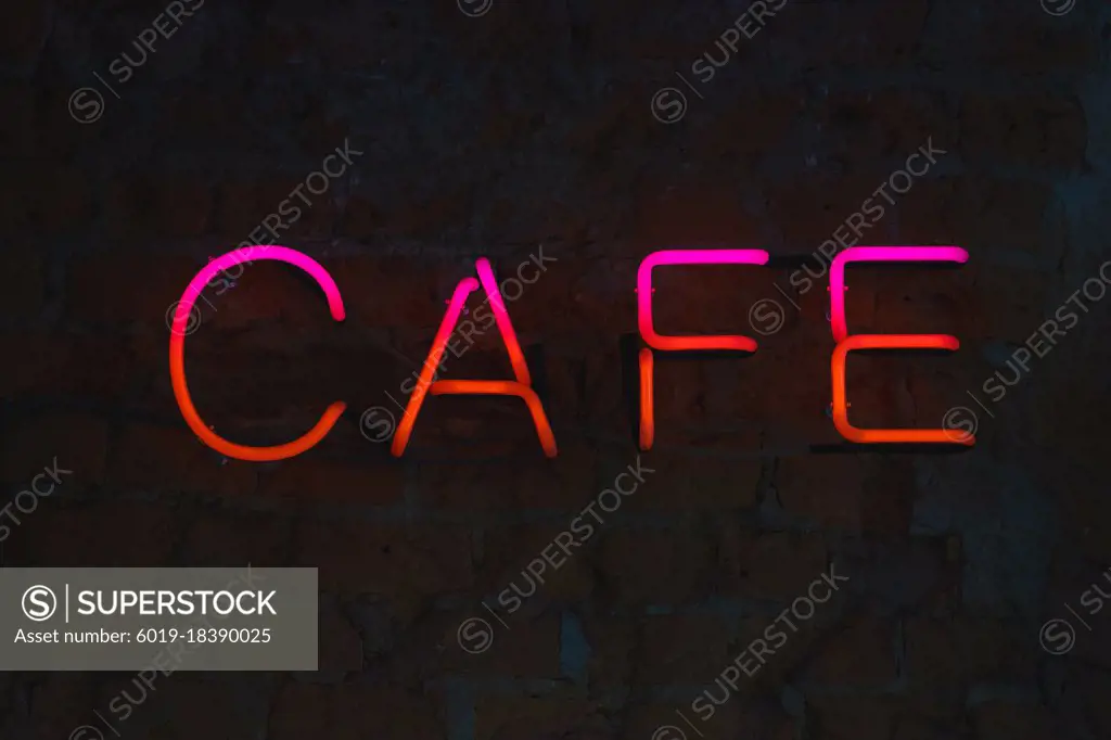 Neon letters, bright signboard cafe on a brick wall close-up.
