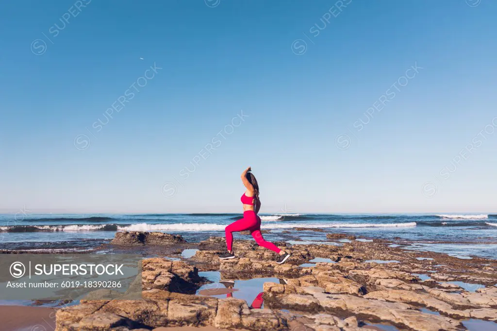 Woman wearing hot pink gym clothes exercising at the beach.