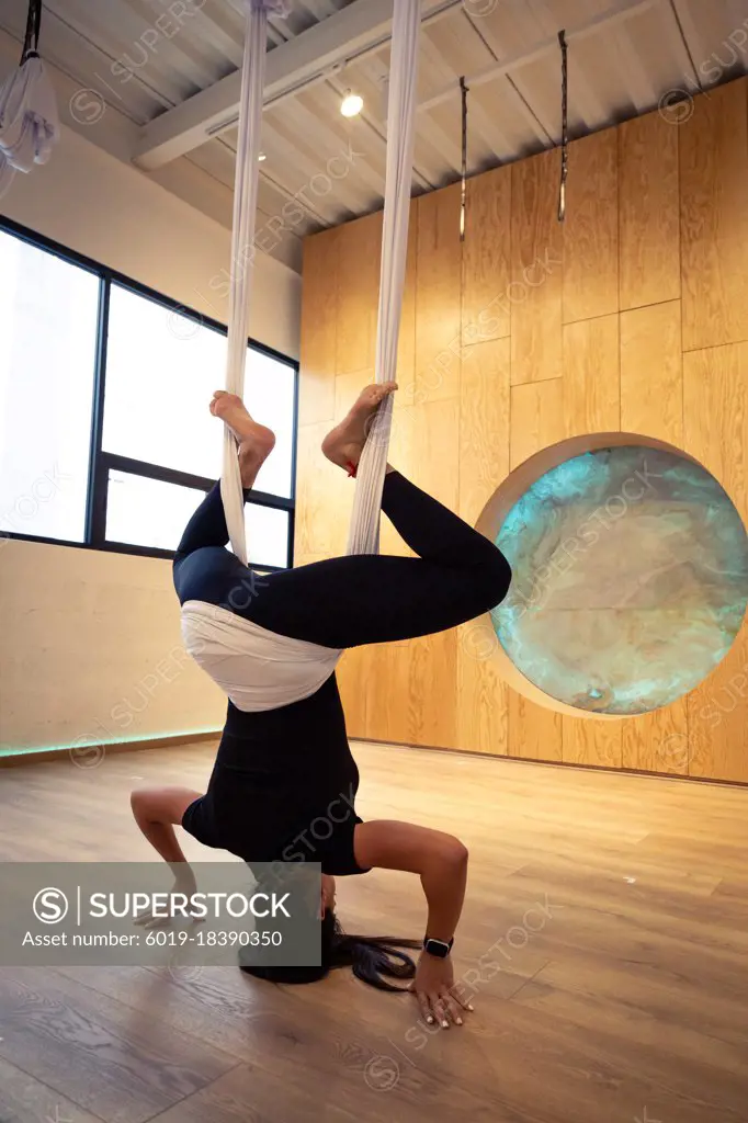 Young woman all in black doing aerial yoga at wooden studio in Mexico