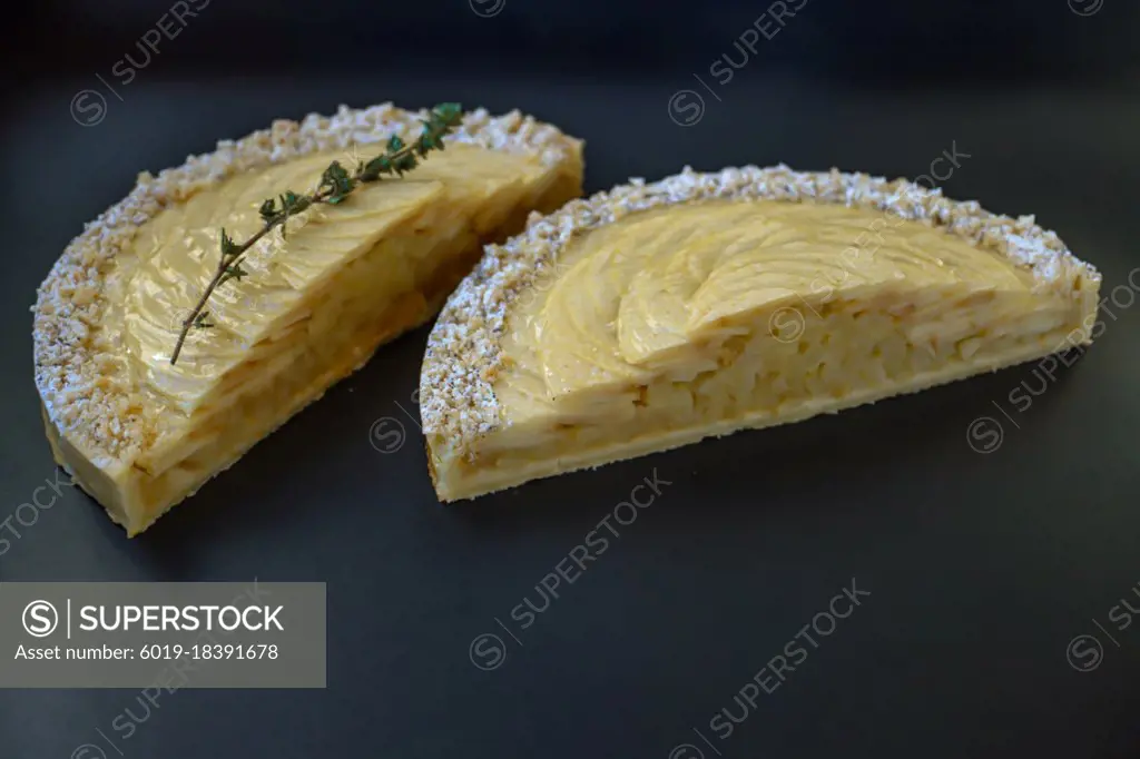 Apple tart cutted in half with green thyme sprig on black font