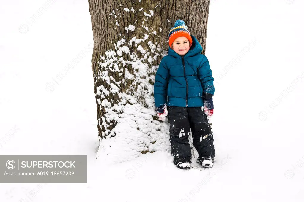 Mischievous boy hiding behind a tree in the snow