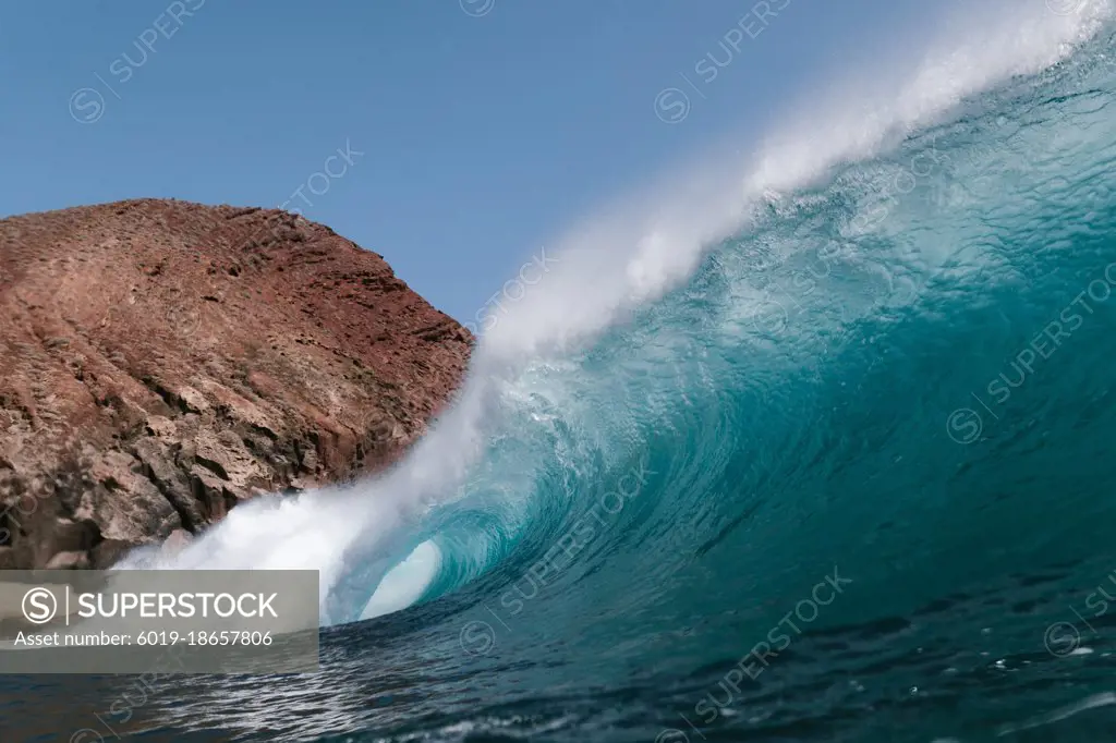 Blue wave breaking front a red mountain in Tenerife