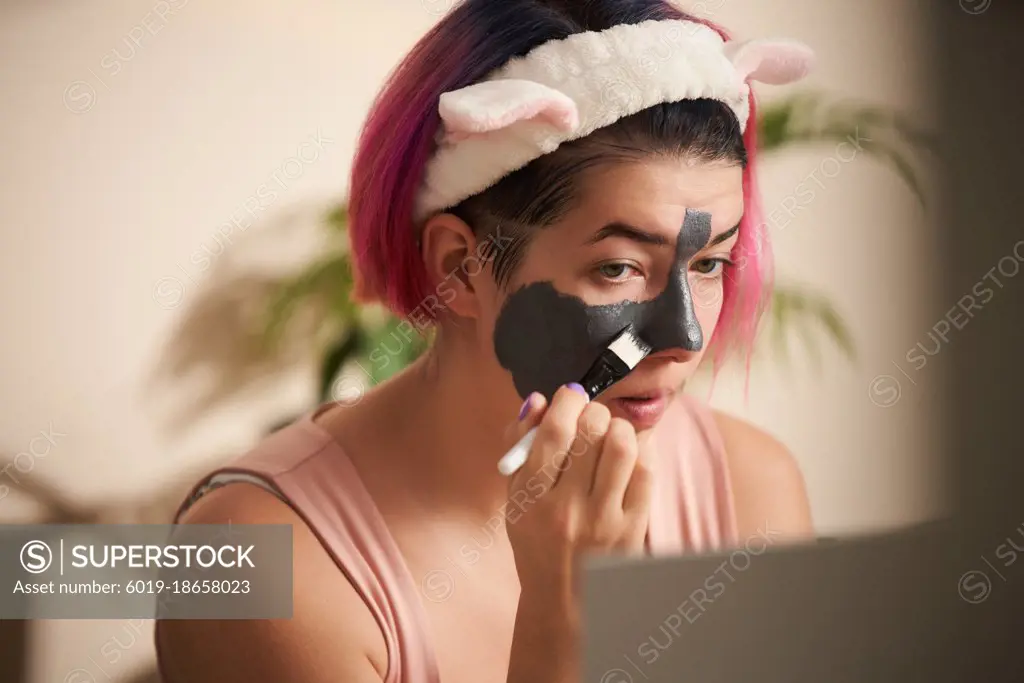 Woman with pink hair inflicts face mask of therapeutic clay.