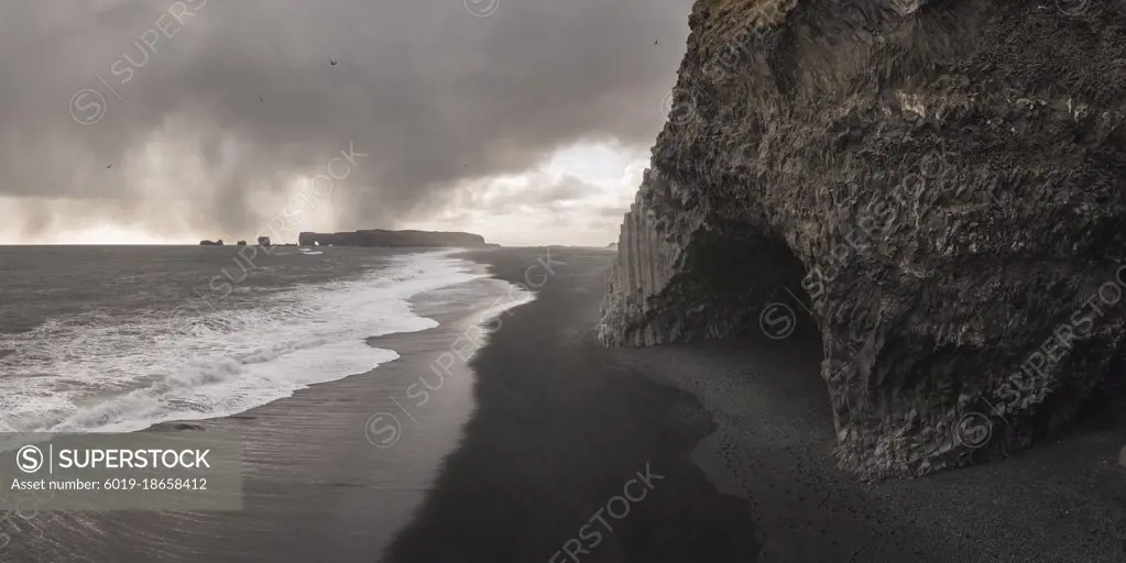 basalt columns cave over black sand beach