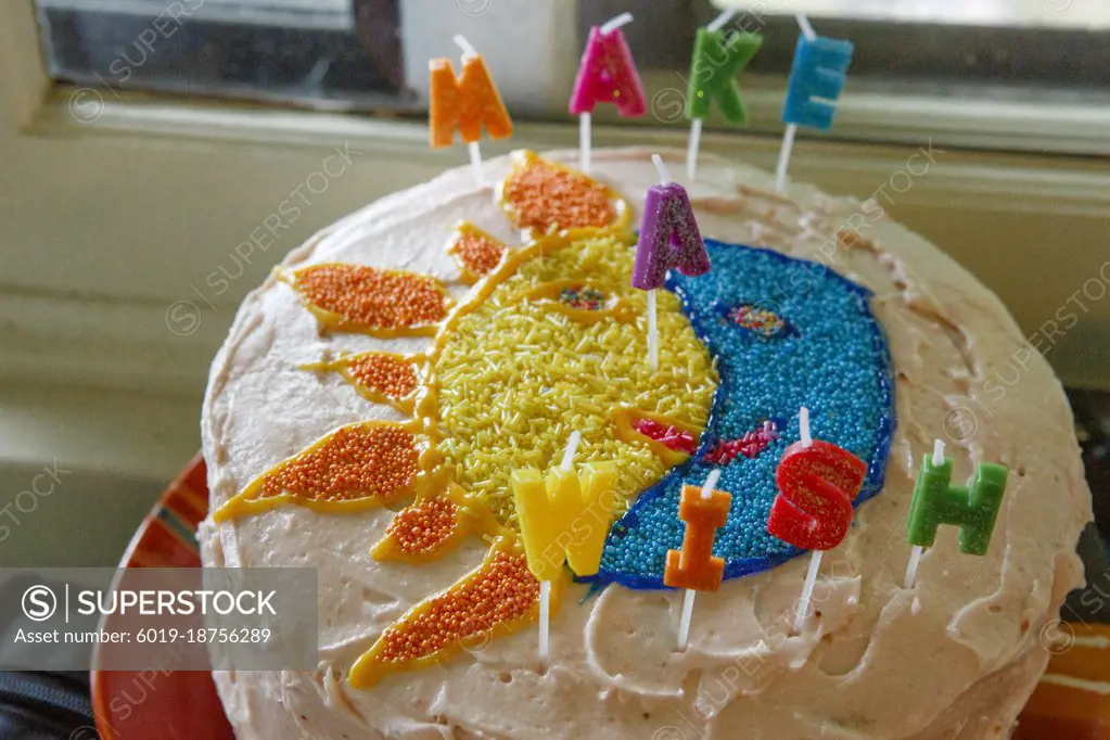 A colorful sun and moon cake with candles that spell "make a wish"