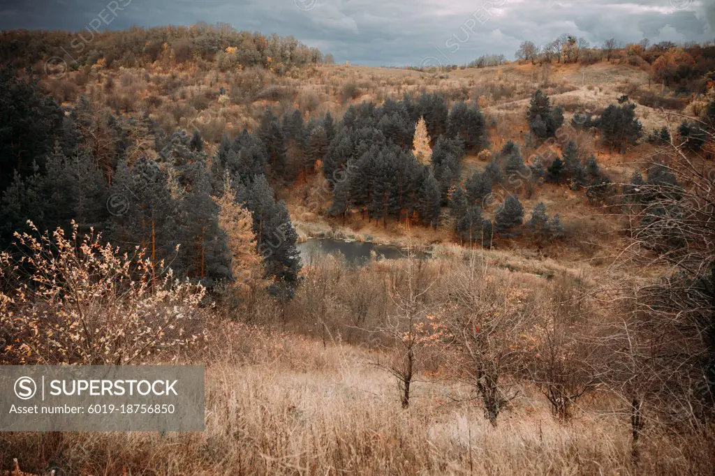 autumn hills with colorful trees and lake under stormy sky