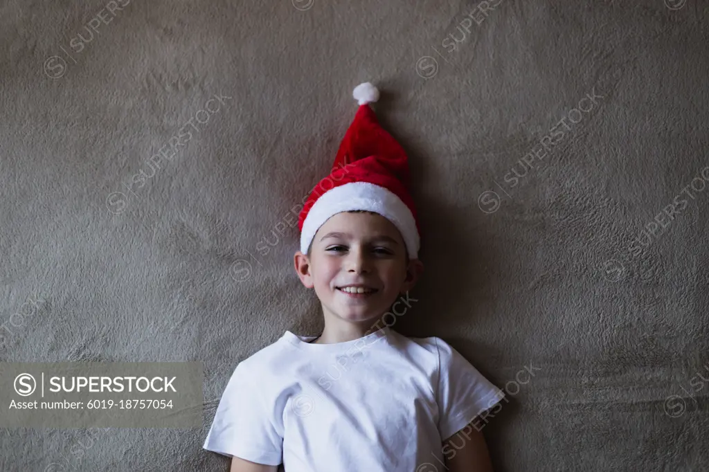 High angle view boy in a Christmas hat smiling while lying on bed