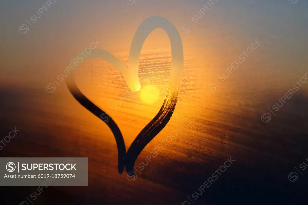 Heart painted on rainy window at sunset