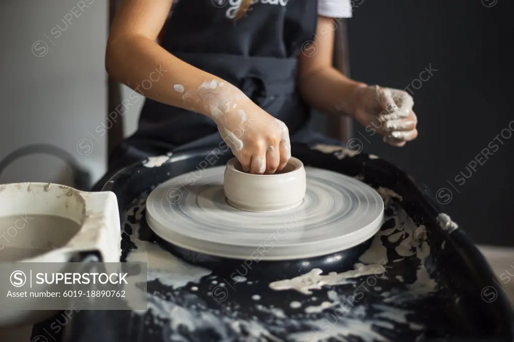 Hands of girl creating bowl on potter's wheel. Traditional craft