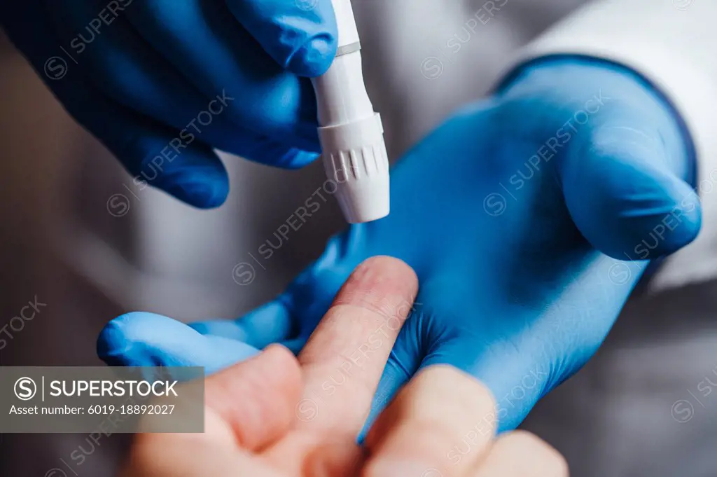 Doctor about to pierce a patient's finger with a lancet