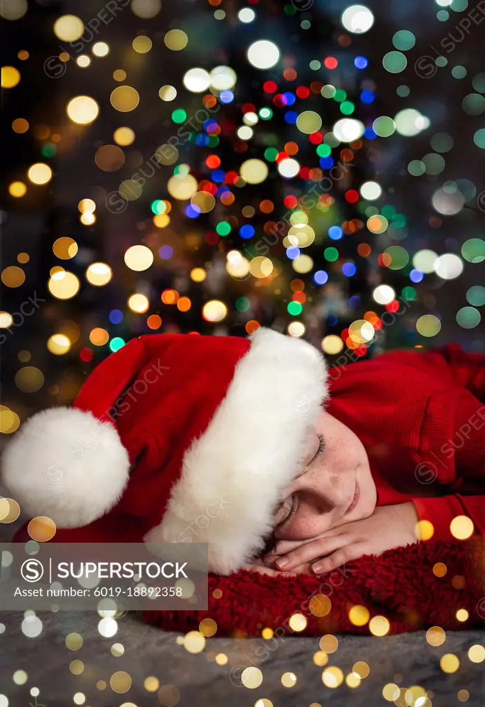 Portrait of boy wearing Santa hat sleeping in front of Christmas tree.