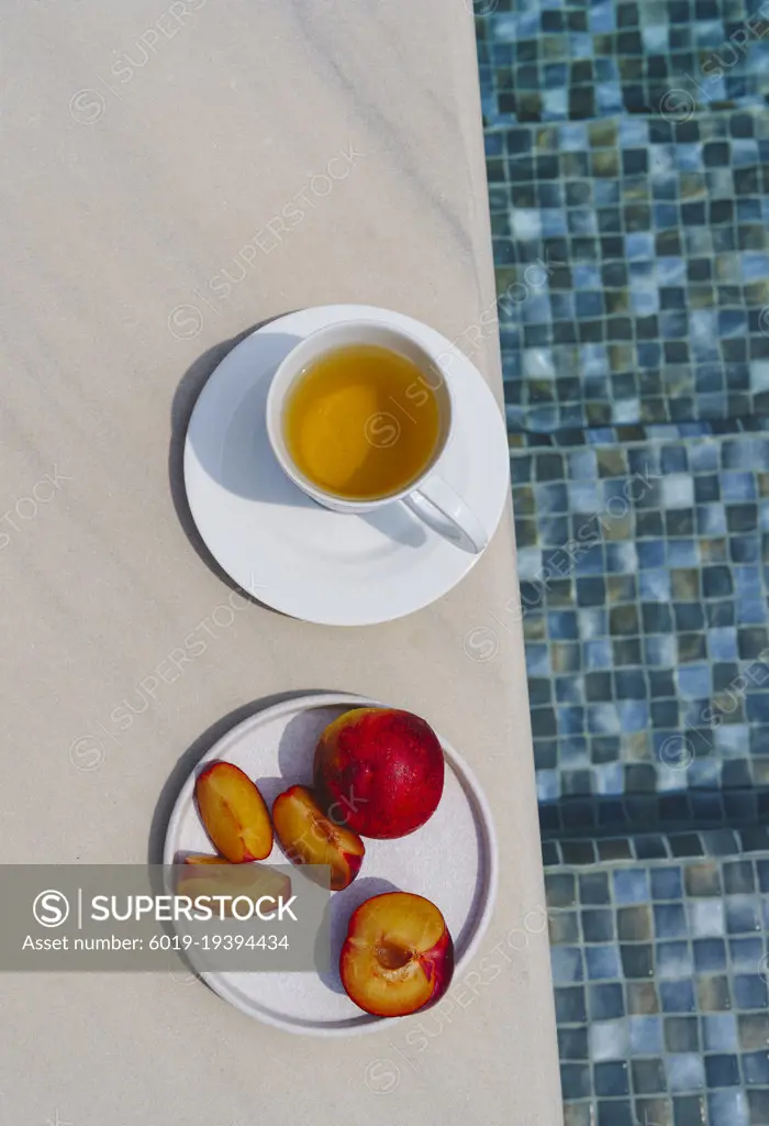 Still life, a cup of tea and a plate of peaches by the pool.