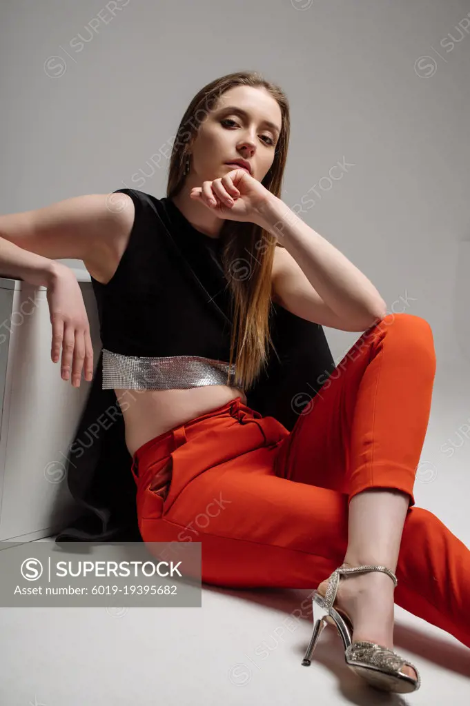 Woman model dressed in red trousers and black jacket posing in studio