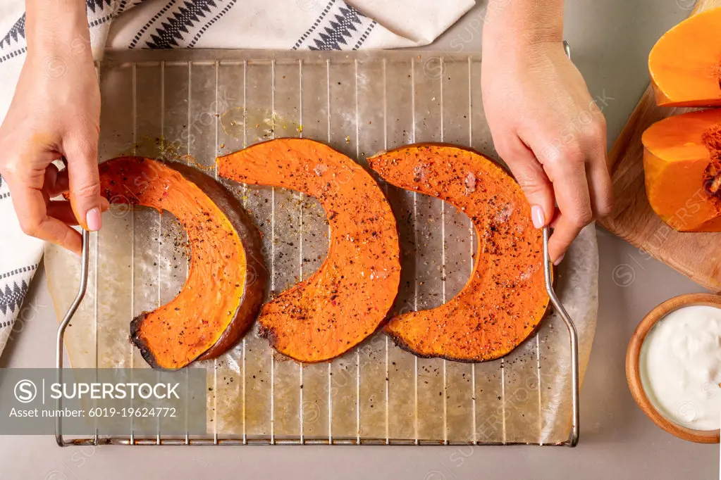 hands holding a tray of baked pumpkin