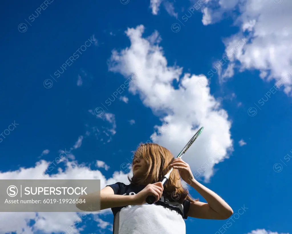 Young girl holding badminton racket with hands on sky background