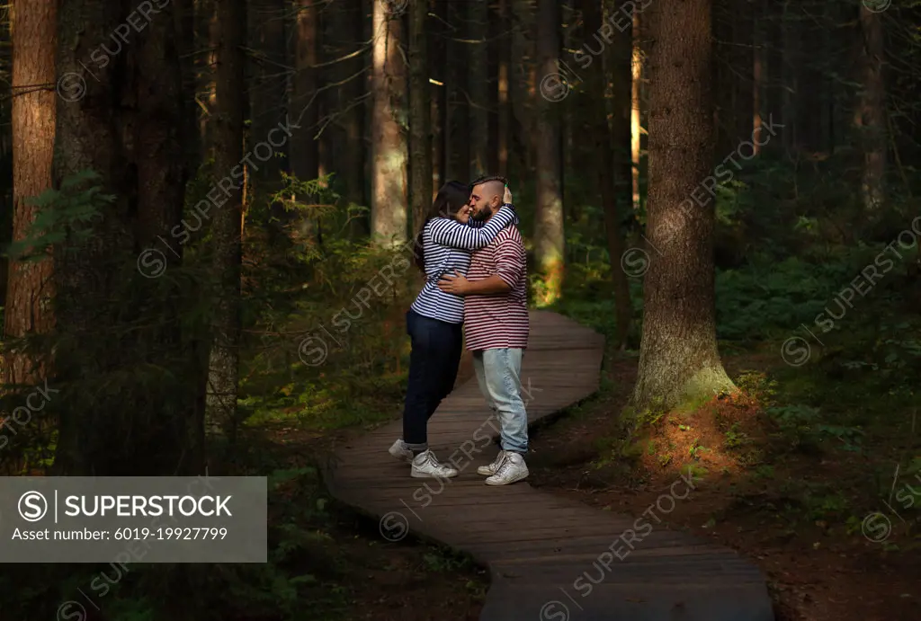 Couple in love hugging on a wooden road in a pine forest