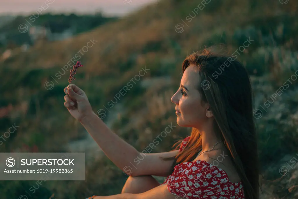 portrait of a young woman in mountains at sunset flower in her hand