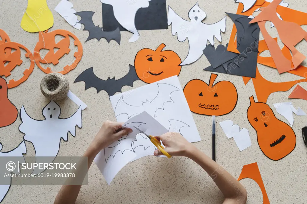 The hands of a girl with scissors make crafts for Halloween.