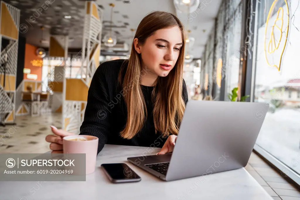 young girl in a cafe by the window working on a laptop