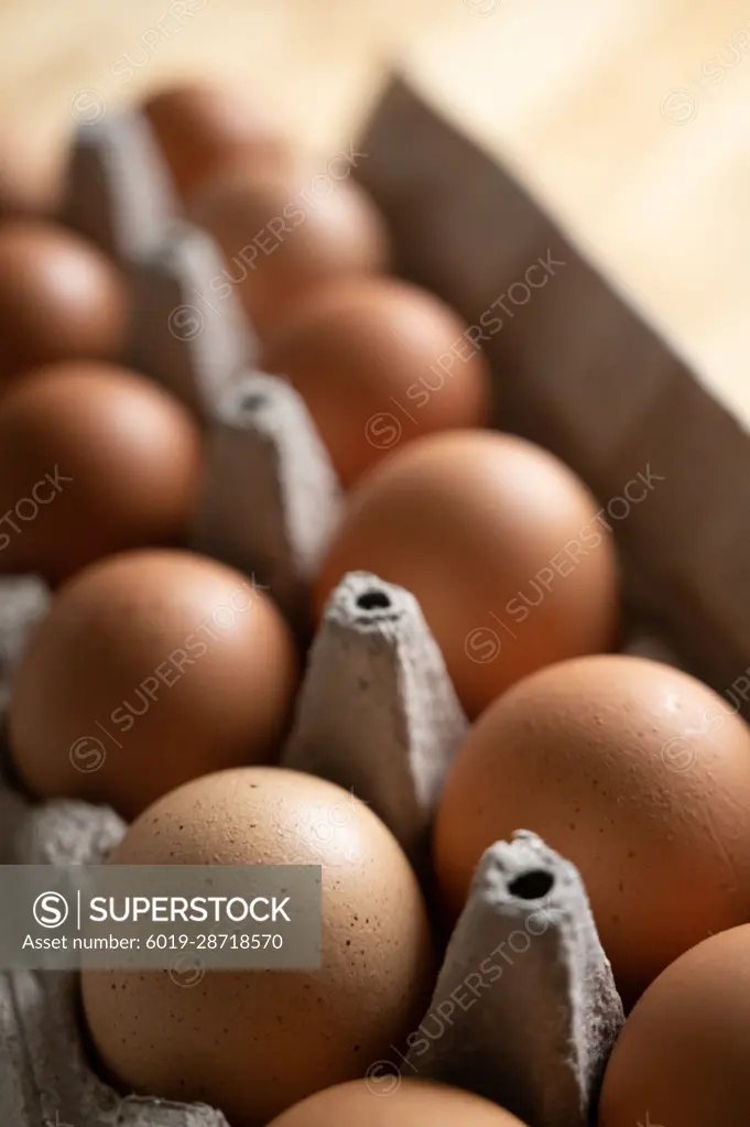 Close up photo of a carton of brown organic eggs on wood kitchen table