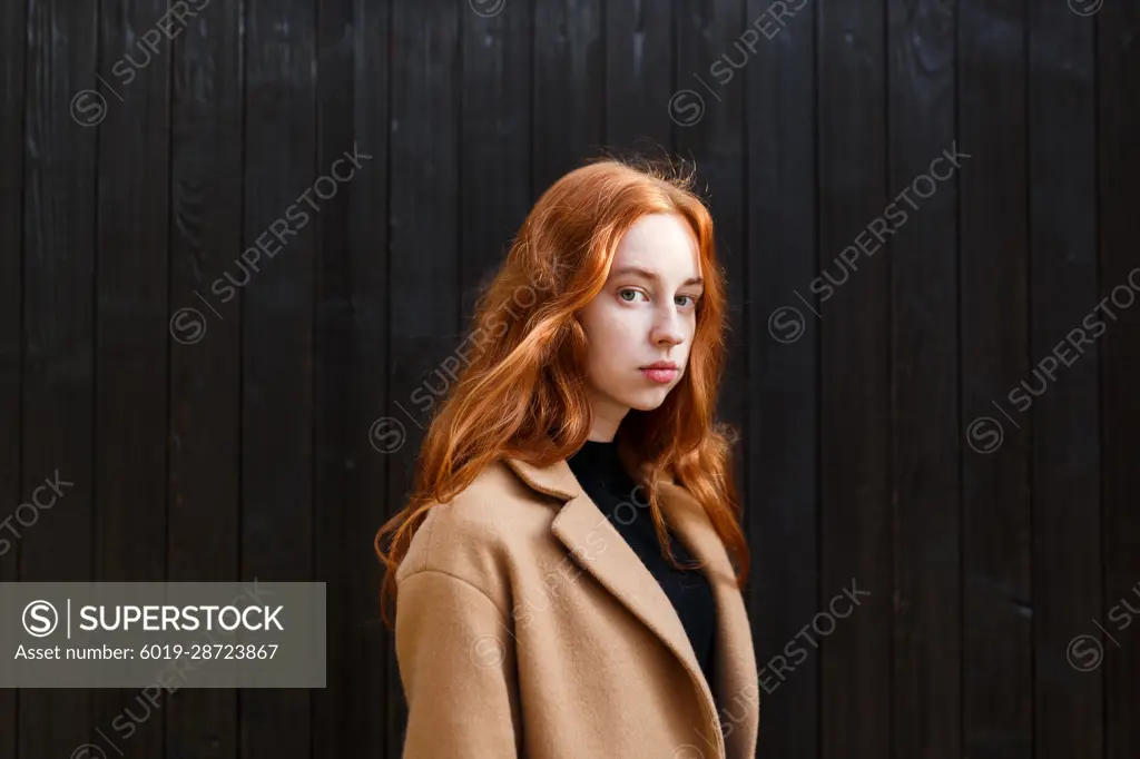 young stylish red-haired woman in a coat near her house in autumn