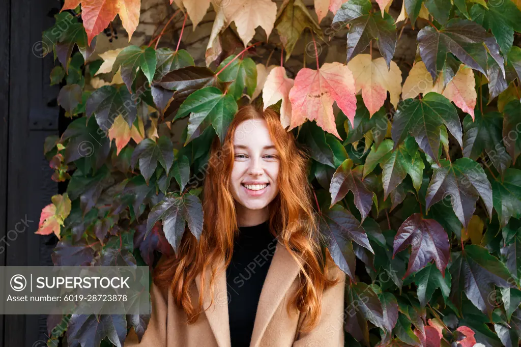 young stylish red-haired woman on the background of green leaves